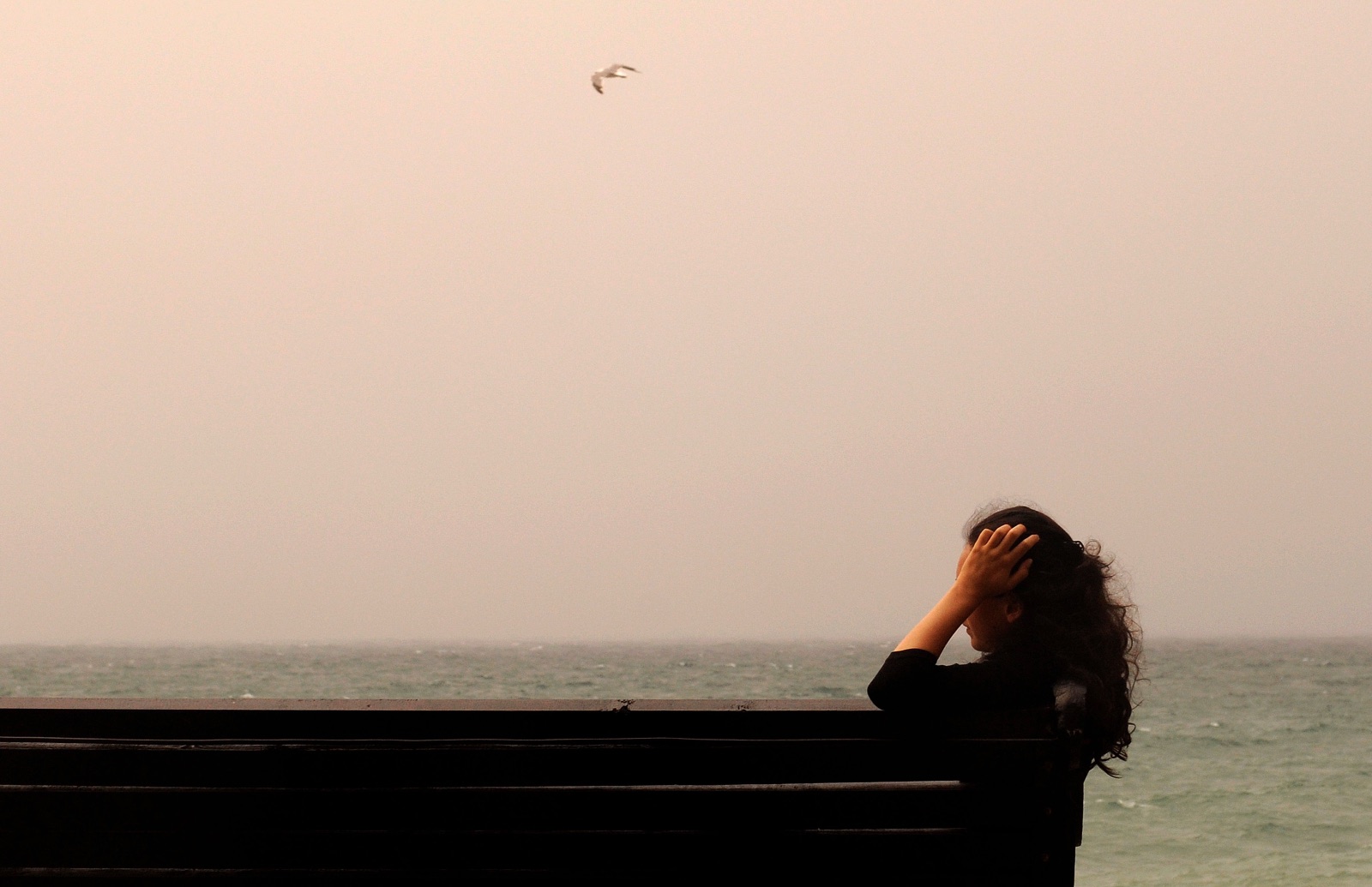 A woman sits alone near the water on a quiet Naples beach, reflecting on the emotional distance she feels in her marriage.