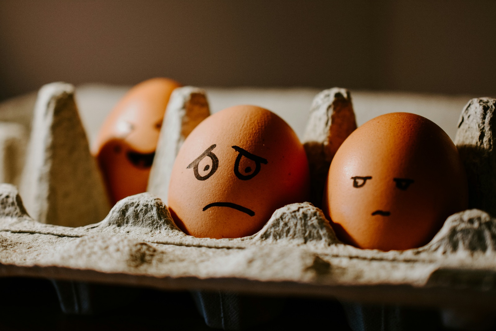 Eggs with faces on them sitting in a carton