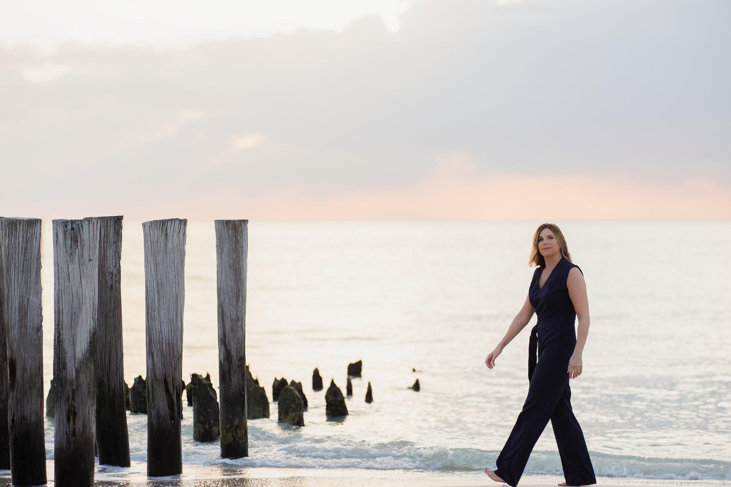 Woman walking along Naples beach at sunset